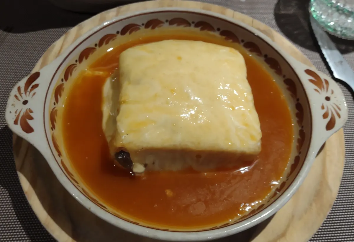 Foto de exemplo: Francesinha com molho num prato de barro